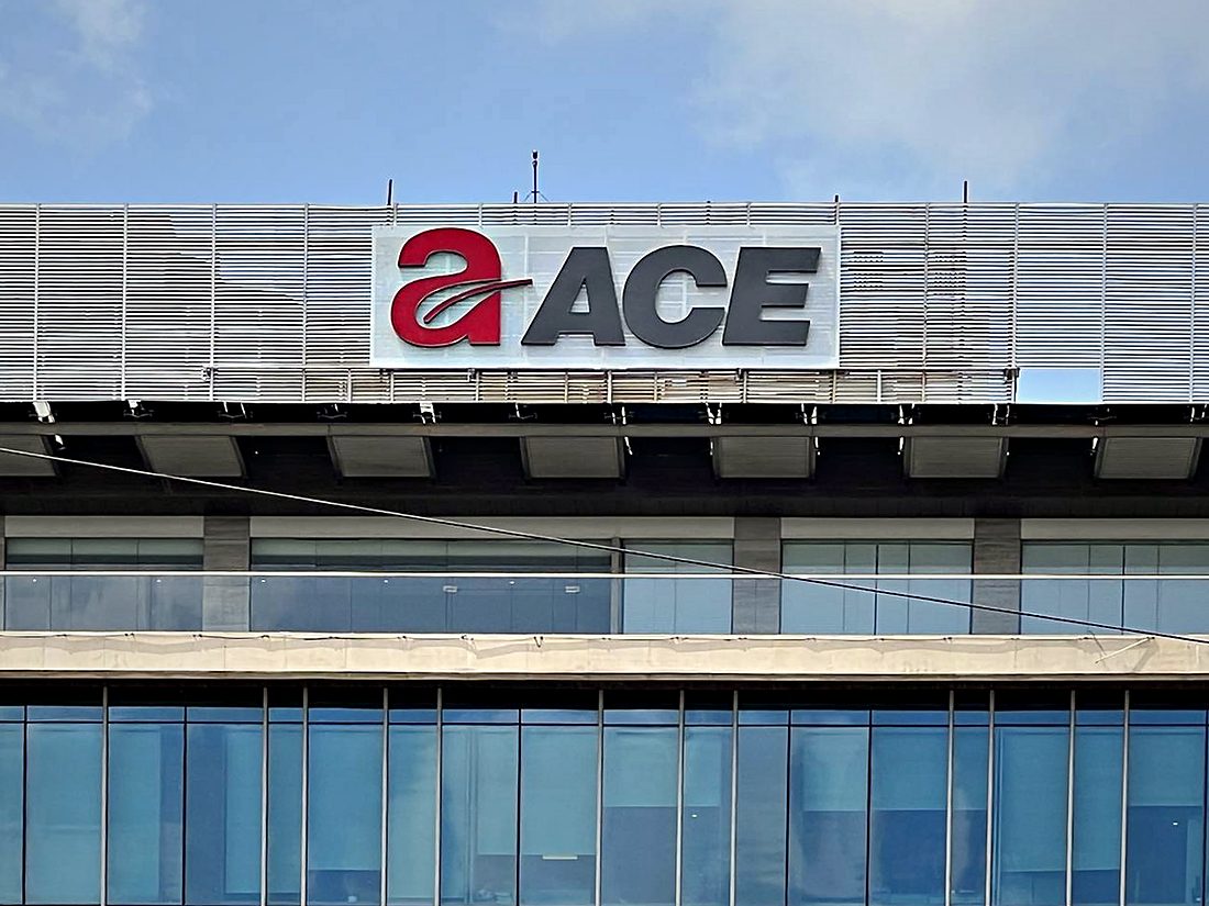 Brand signage mounted on a perforated ACP screen above a glazed office frontage, carried on its own sub-frame clear of the curtain wall.