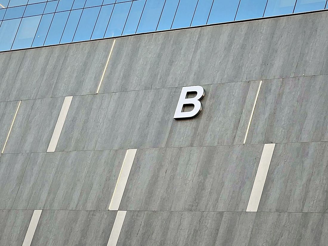 Individual dimensional letter fixed to a stone-finish facade panel and aligned to the cladding joints, so the signage reads as part of the elevation.