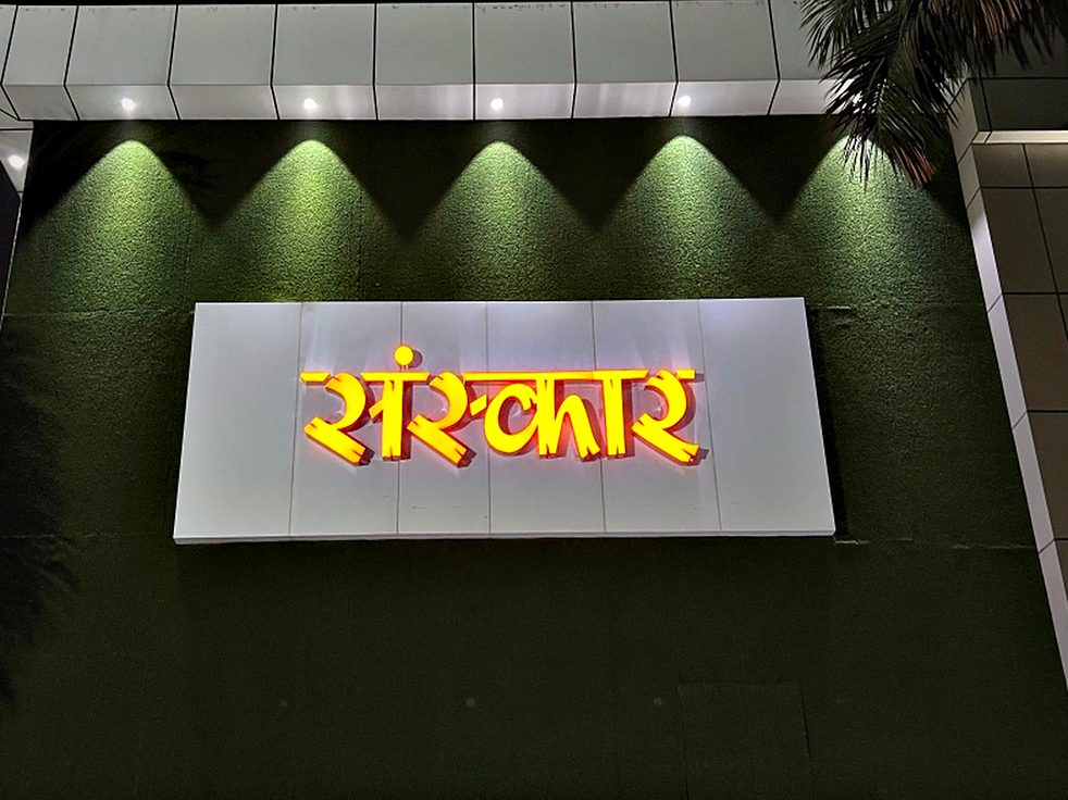Face-lit Devanagari lettering on a raised panel, with a cove wash behind it to lift the whole feature off the wall.