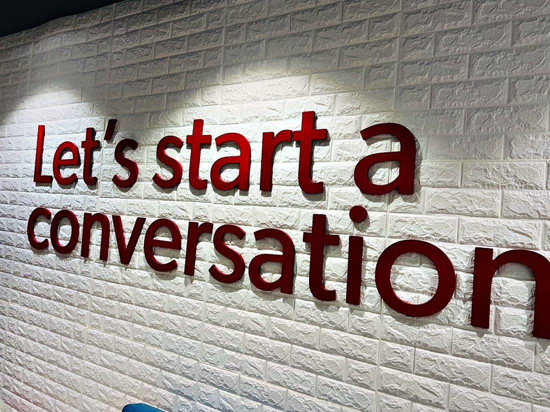 Dimensional red lettering on a textured white brick reception wall, lit from above to throw a soft shadow.