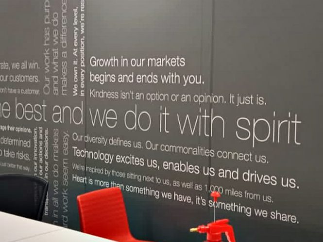 Full-height brand narrative applied as cut vinyl typography across a dark office wall.