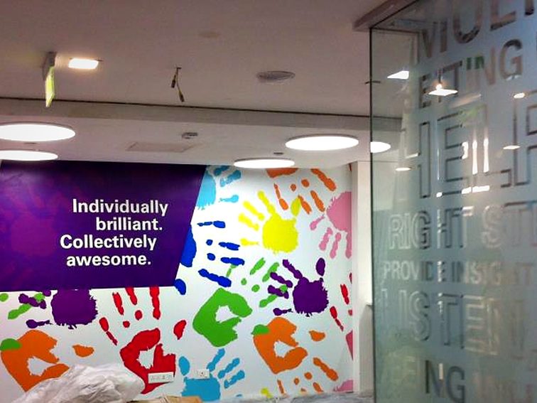 Printed culture wall combining a brand statement panel with a colour handprint mural across the corridor.