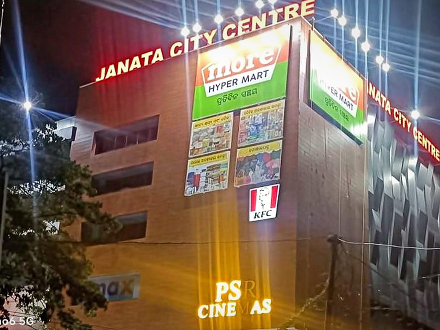 Illuminated mall facade signage — anchor-brand boxes and cinema branding lit for night-time visibility from the highway.