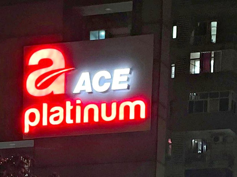 Face-lit acrylic brand signage on a residential tower, sized and lit to read clearly from the approach road.