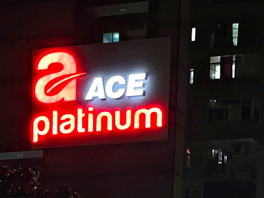 Face-lit acrylic brand signage on a residential tower, sized and lit to read clearly from the approach road.