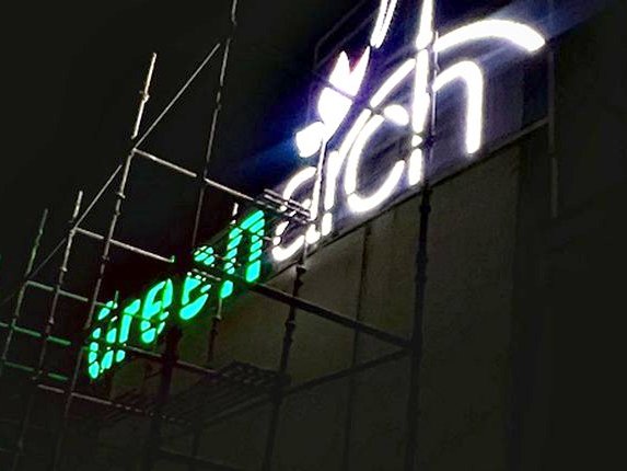 Rooftop identification signage on a steel support frame, illuminated so the name holds against a dark skyline.