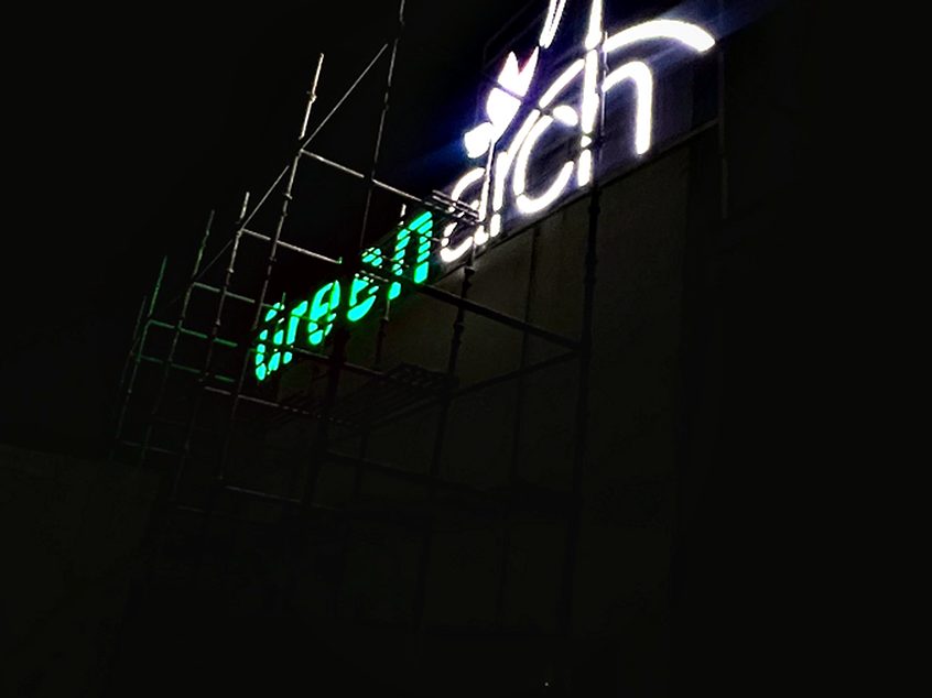 Rooftop identification signage on a steel support frame, illuminated so the name holds against a dark skyline.