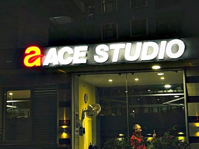 Face-lit brand lettering above a glazed studio frontage, bright enough to carry the shop line after dark.