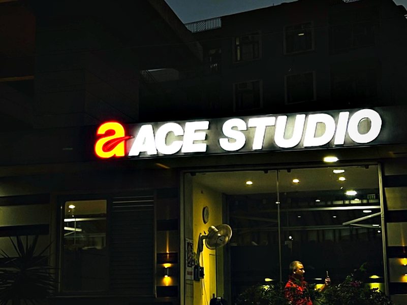 Face-lit brand lettering above a glazed studio frontage, bright enough to carry the shop line after dark.