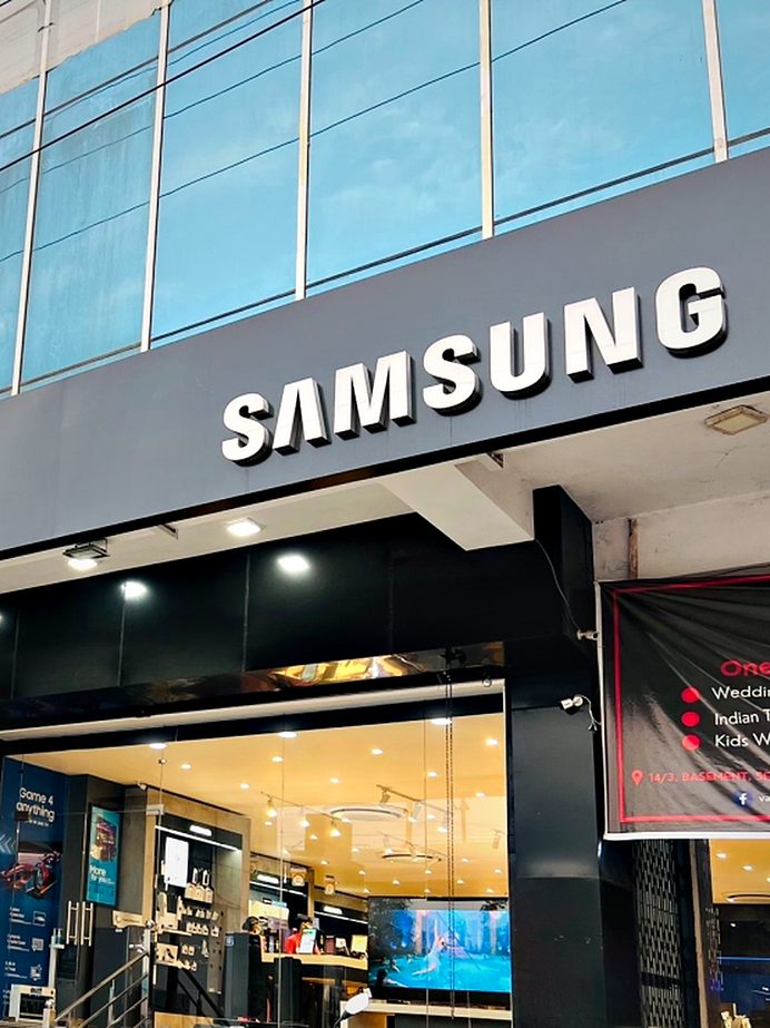 Illuminated brand fascia over a glazed retail frontage, with campaign graphics worked into the shop window line.