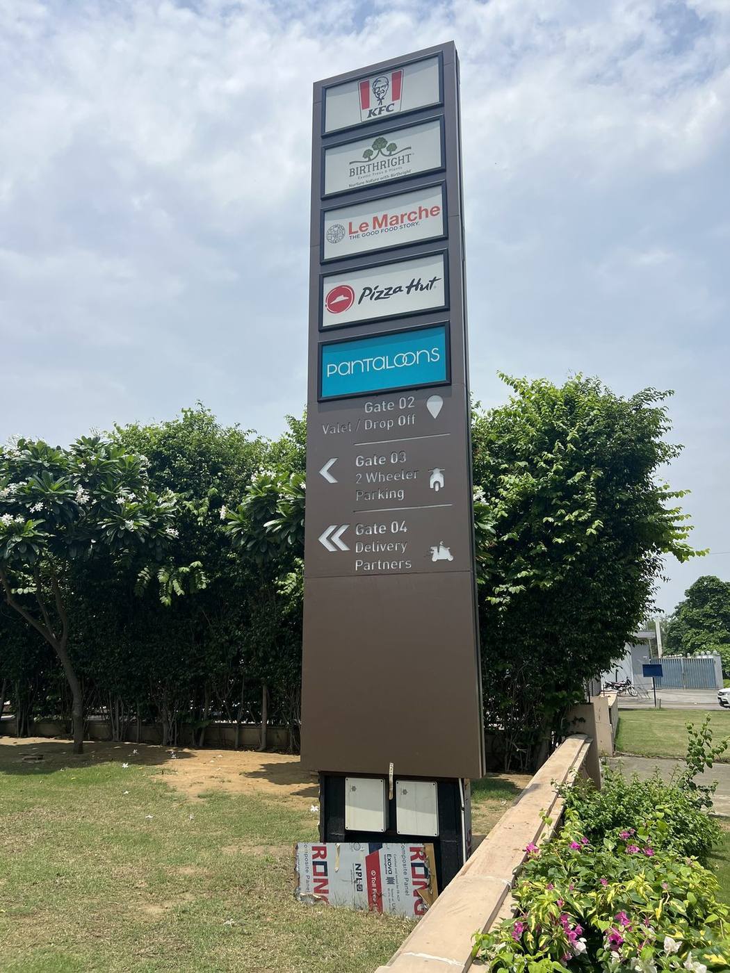 Tall multi-brand directory totem carrying anchor retail and F&B tenants on individually backlit panels within a powder-coated steel frame.