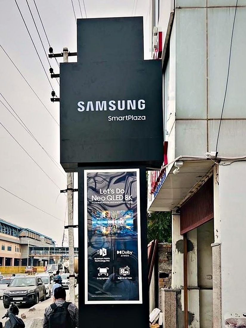 Roadside identification pylon for a Samsung SmartPlaza, with a backlit brand box above a lit campaign panel sized for approaching traffic.