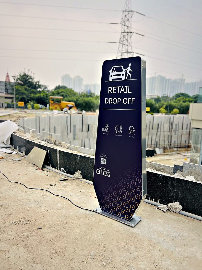 Drop-off zone totem with a laser-cut patterned base and a clear directional panel for arriving shoppers.