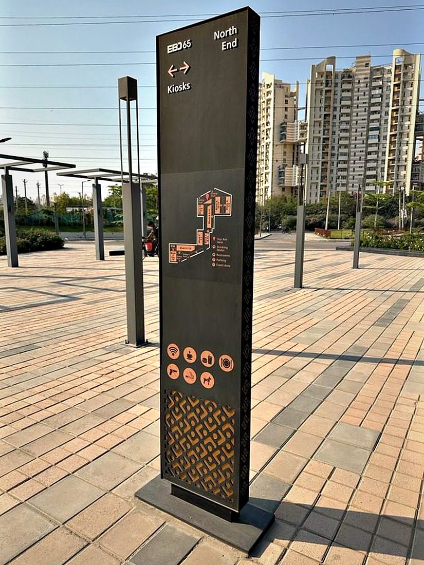 Freestanding directory totem set in a landscaped plaza, listing tenants and amenities for a mixed-use retail destination.