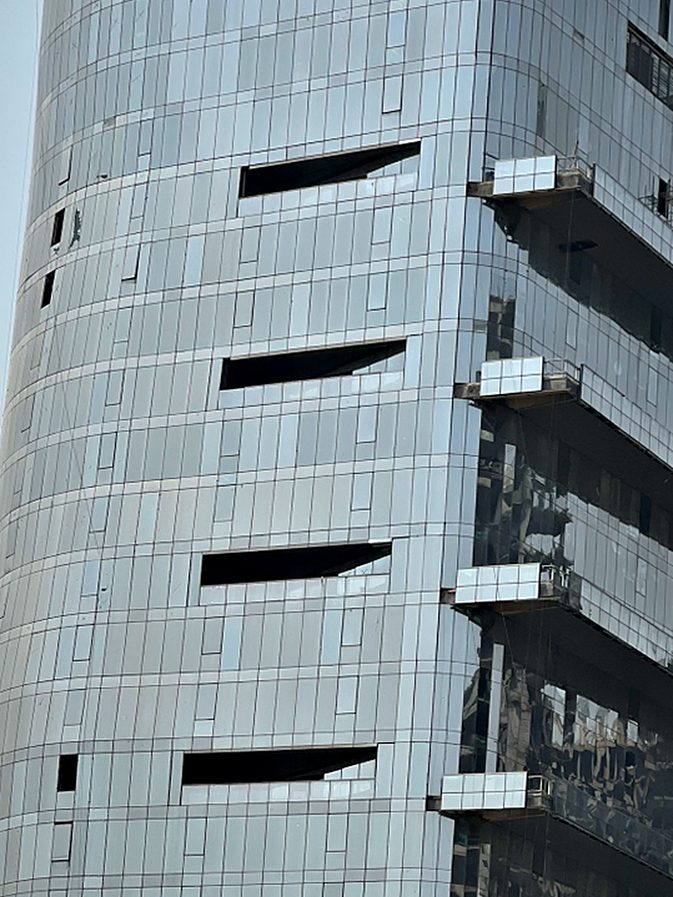 Tower identification signage on a curved stone-and-glass elevation, set high on the shaft where it reads from the arterial road.
