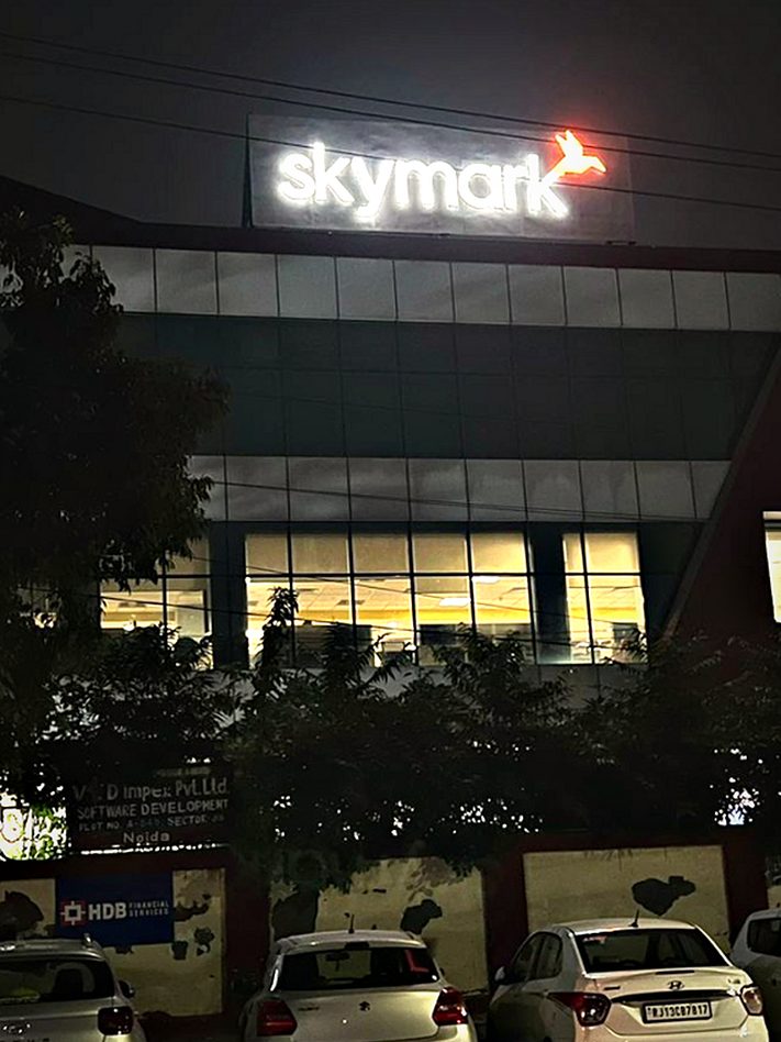 The same tower identity after dark — rooftop signage lit so the name holds above the surrounding skyline.