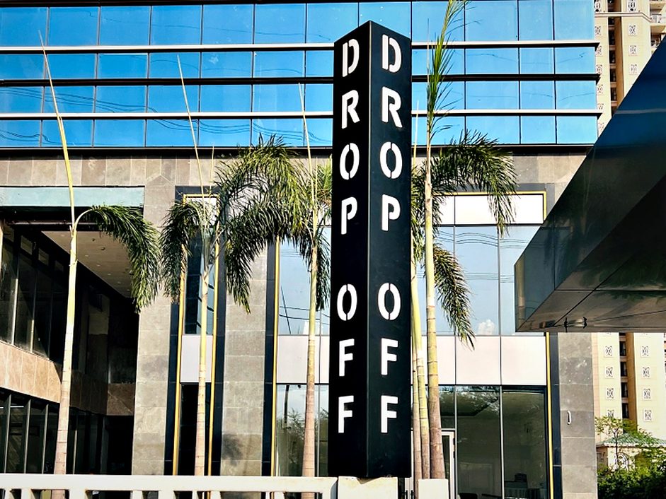 Double-sided vertical blade signage marking the drop-off point at a glass-fronted corporate tower, sized to be read from the approach road.