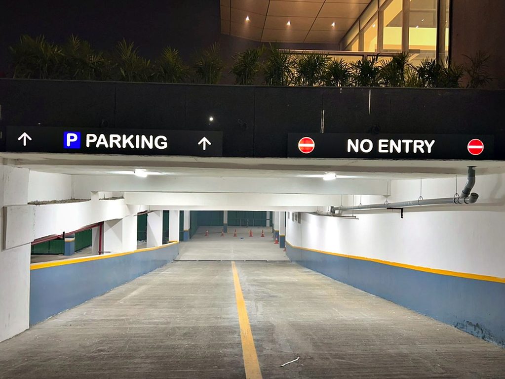Backlit fascia signage over a basement ramp, separating the parking entry from the no-entry lane to keep traffic one-way.