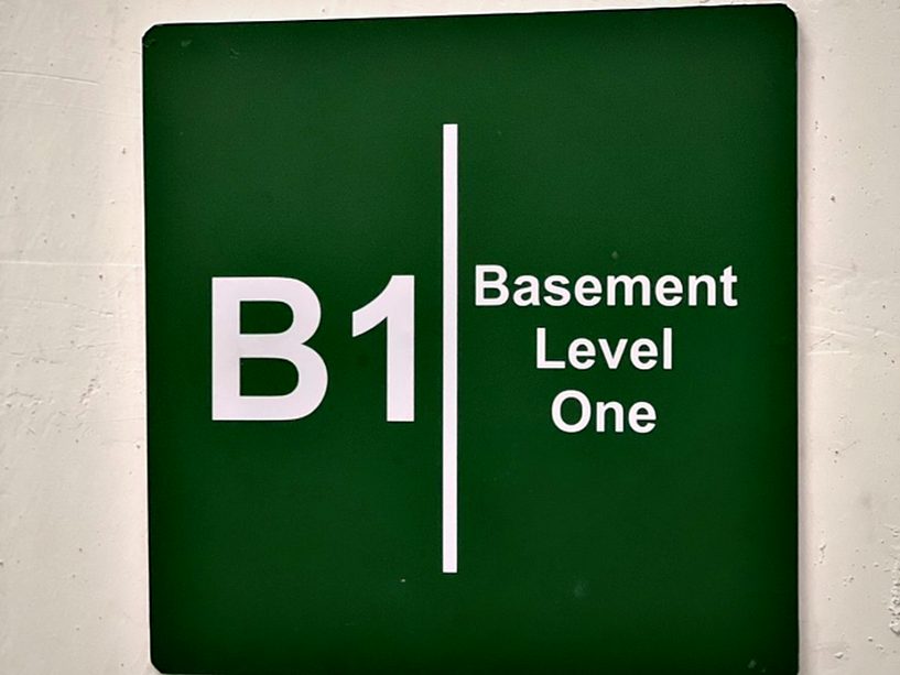 Level-identification plate for basement one in high-contrast white on green, chosen to stay readable under low car-park lighting.