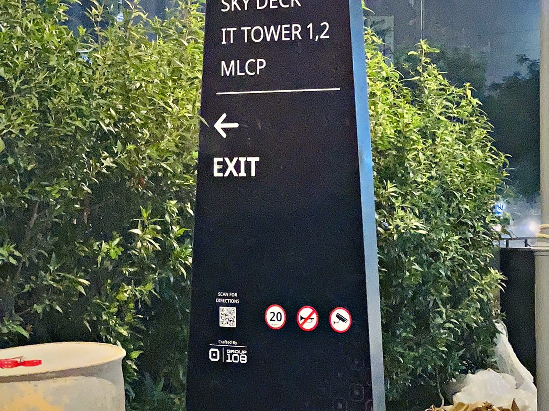 Freestanding campus wayfinding totem routing visitors to the sky deck, IT towers, multi-level car park and exit, with a QR code for turn-by-turn directions.